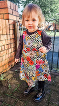 Child wearing a colorful floral dress standing outdoors near a brick wall.